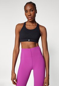 Schwarzer Sport-BH mit Criss-Cross-Rücken und weißem Logo, kombiniert mit hochgeschnittenen, leuchtend pinken Leggings mit sauberen Nähten und glatter Textur.