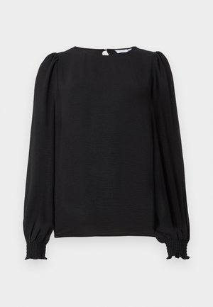 Melnā blūze ar garām uzpūstām piedurknēm. Ražota ar noapaļotu dekoltē, aizmugures atslēgas formas atvērumu un smock-velkām aprocēm, kas nodrošina pieguļošu izskatu. Gluda tekstūra.