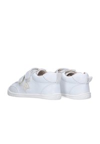Par de zapatillas blancas pequeñas para niños con tiras de Velcro, vistas desde la parte trasera sobre un fondo blanco.