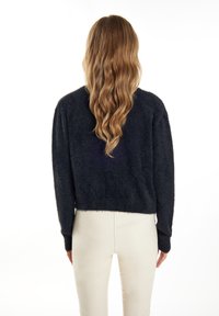Svart, fluffig kort tröja med långa ärmar, som har en rund halsringning och ribbade manschetter. Bärs över ljusa, figurnära byxor.