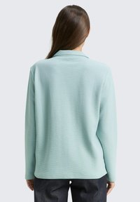Hellblaues Langarmhemd mit Kragen, strukturiertem Material und lockerer Passform, kombiniert mit dunklen Jeans.