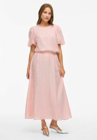 Lyserød kjole med tekstureret stof, korte puffærmer og en flydende nederdel. Sølv sko komplementerer outfittet.