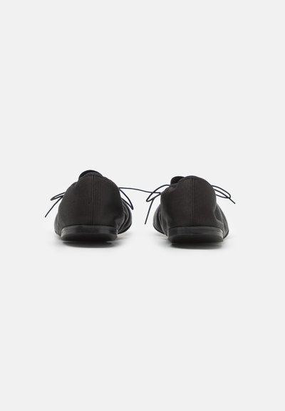 Zapatos casuales negros con parte superior de textil suave, puntera redondeada y suela plana. Cuentan con cordones finos y un diseño minimalista.