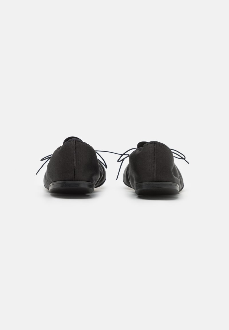 Zapatos casuales negros con parte superior de textil suave, puntera redondeada y suela plana. Cuentan con cordones finos y un diseño minimalista.