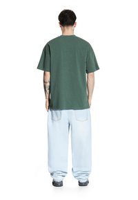 Zielona bawełniana koszulka z luźnym krojem i krótkimi rękawami, zestawiona z jasnoniebieskimi, workowatymi dżinsami. Tył nie ma widocznych logo ani wzorów.