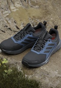 Czarno-niebieskie buty sportowe z teksturowaną cholewką, wspierającym dopasowaniem i wzmocnioną podeszwą, zaprojektowane do aktywności na świeżym powietrzu, z oznaczeniem "ClimaProof".