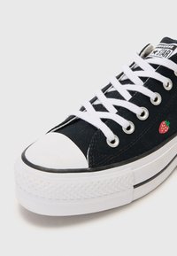 Musthave mustkanna sneakers musta värviga valge ninaosas ja tallaga, millel on valged paelad ja väike punane maasika tikand külje peal.