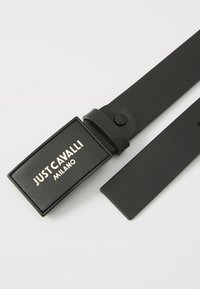 Svart lærbelte med en rektangulær spenne som har gulltekst "JUST CAVALLI MILANO." Jevn tekstur og minimalistisk design.