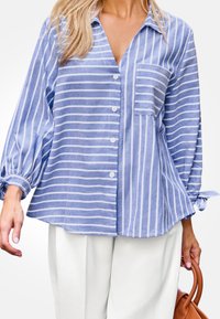 Blau gestreiftes Hemd mit lockerer Passform, langen puffärmeln und einer Brusttasche. Mit einer Knopfleiste und gebundenen Akzenten an den Ärmeln.