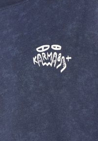 T-shirt in cotone blu navy con un design grafico bianco caratterizzato da simboli astratti e la scritta "KARMA8+" sul lato sinistro. Texture morbida, collo a giro.