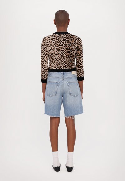 Pulover cu imprimeu leopard și margini negre, asociat cu pantaloni scurți din denim albastru deschis cu margini desfăcute și două buzunare pe spate. Pantofi negri și șosete albe.