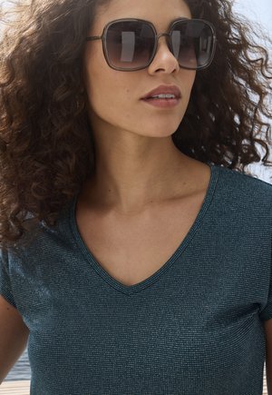 Teal V-neck top featuring short sleeves and a textured fabric with subtle stripes. Large dark sunglasses complete the look.