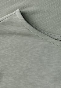 Světle zelená látka s hladkou texturou, s kulatým výstřihem a viditelnými švy.