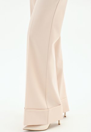 Pantalon beige à jambes larges avec un grand revers, porté par-dessus des escarpins à bouts pointus, vu de mi-mollet jusqu'aux pieds.