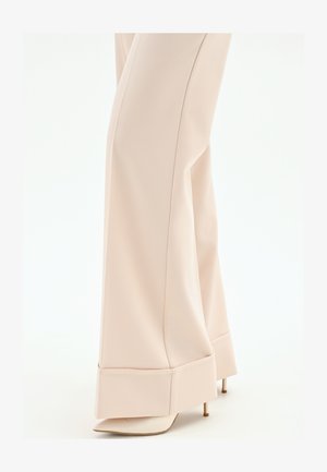 Pantalon beige à jambes larges avec un grand revers, porté par-dessus des escarpins à bouts pointus, vu de mi-mollet jusqu'aux pieds.