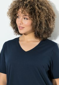 T-shirt col en V bleu marine fabriqué en tissu doux avec des manches courtes. Présente une coupe décontractée et une texture lisse.