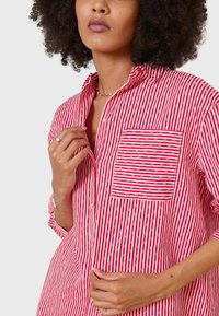 Red and white striped shirt with a collared neckline, button front, and a chest pocket. Fabric appears lightweight and textured.