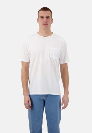 T-shirt bianca in cotone con colletto rotondo, maniche corte e taschino frontale. Abbinata a jeans in denim azzurri. Texture minimale.