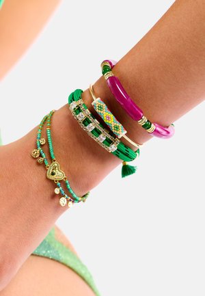 Pile colorée de bracelets, comprenant un jonc rose, un bracelet à perles multicolores, des styles tissés verts, et des accents dorés avec des breloques.