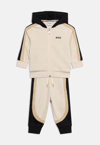 Σετ φόρμας για νήπιο σε μπεζ, μαύρο και ταμπά με ζακέτα με φερμουάρ και παντελόνι με ελαστική μέση, με το λογότυπο BOSS στο στήθος και στο μπατζάκι του παντελονιού.