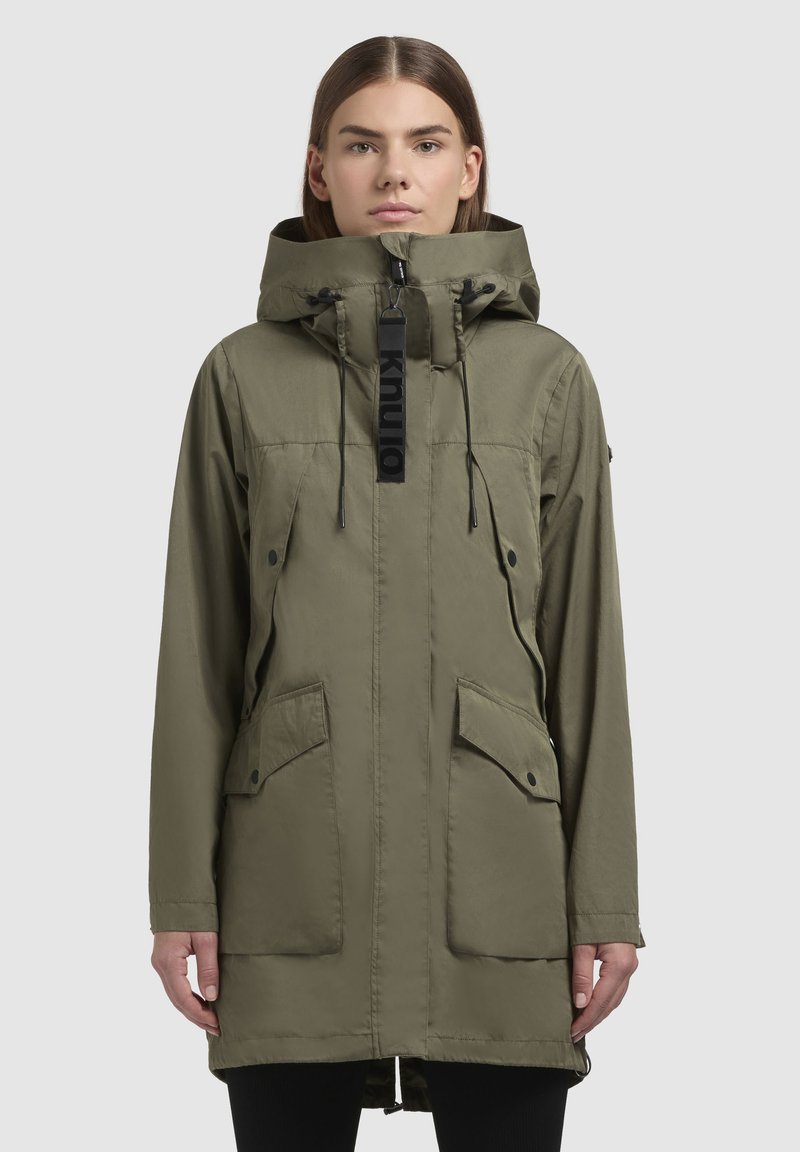 Parka en vert olive avec capuche à cordon de serrage, zip à l'avant, poches à pression et une étiquette logo audacieuse au niveau du cou. Tissu lisse et léger.