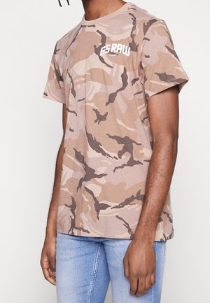 Koszulka z krótkim rękawem w kolorze beżowym w wzór moro, wykonana z mieszanki bawełny, z białą grafiką logo na klatce piersiowej i luźnym krojem.