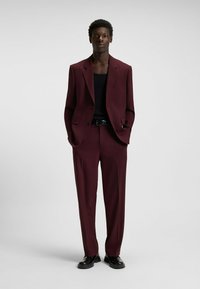 Maroon suit with a structured blazer and straight-leg trousers, paired with a black tank top and black shoes; smooth texture and tailored fit.