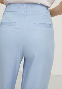 Pantalons bleu clair avec une texture lisse, taille haute et deux poches arrière. Présente un design ajusté et des lignes épurées.