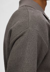 Polo à manches courtes en gris texturé avec un col côtelé et des coutures d'épaule. Fabriqué en tissu tissé doux.