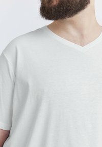 Hvid v-hals t-shirt i blødt stof, med korte ærmer og en afslappet pasform, med subtil tekstur synlig på overfladen.