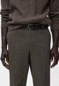 Suéter marrón de punto acanalado combinado con pantalones texturizados verde oliva, con un cinturón de cuero negro con hebilla plateada.