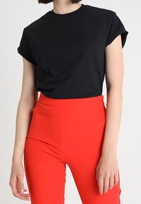 Černé tričko s krátkým rukávem a přehnutými manžetami spárované s vysokými červenými kalhotami, které mají hladkou strukturu a dobře padnoucí střih.