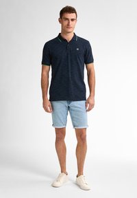 Camisa polo a rayas marino con detalles en verde, combinada con pantalones cortos de mezclilla clara y zapatillas beige. Tejido de algodón, corte clásico.