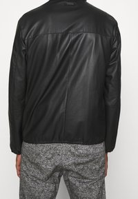 Svart läderjacka med en slät yta, elastiska muddar och rak skärning. Har en sömdetalj som går tvärs över ryggen.