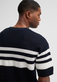 Marineblau gestrickter Pullover mit horizontalen weißen Streifen, Rundhals, kurzen Ärmeln, strukturiertem Gewebe und gerippten Bündchen.