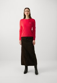 Red knit sweater with ribbed hem and cuffs, paired with a long brown denim skirt featuring a side slit. Black ankle boots complete the look.