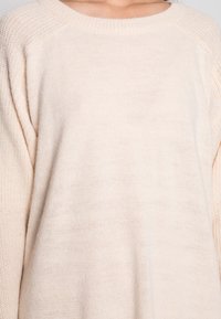 Maglione lavorato a maglia beige chiaro con colletto rotondo, caratterizzato da un motivo testurizzato e maniche raglan per un fit rilassato. Polsini a coste spessi.