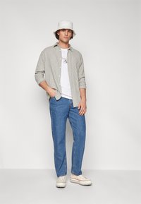 Checkered beige shirt, white t-shirt, blue jeans, and white bucket hat. Simple sneakers with a textured sole complete the outfit.