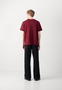 Maroon majica s kratkim rukavima, okrugli izrez, opušteni kroj, uparena s tamnim širokim hlačama. Jednostavan dizajn, bez vidljivih uzoraka ili naglasaka.