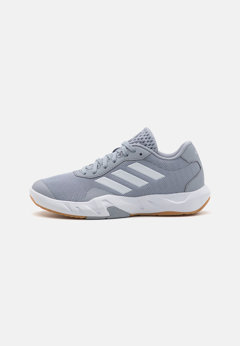 Zapatillas deportivas grises con parte superior de malla, tres franjas blancas, cuello acolchado y suela de goma, con un diseño texturizado para mayor agarre.