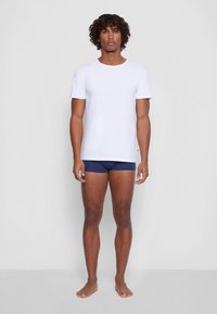 Fehér rövid ujjú póló sötétkék alsóneművel párosítva. Normál szabású, puha pamut anyagból, sima textúrájú, látható mintázat nélkül.