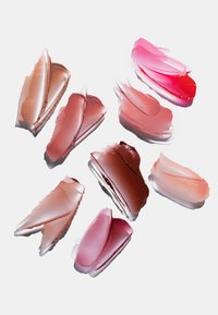Diverses taches de rouge à lèvres ou de gloss dans des teintes de rose, nude et rouge sur fond blanc.