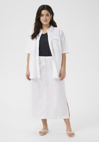 Witte blouse over een zwarte top, in combinatie met een witte maxi rok met zijsplits. Lichte sandalen passen bij de outfit.