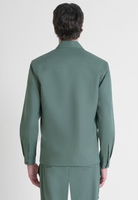 Camicia a maniche lunghe ricca di texture in un verde tenue, con colletto classico e polsini con bottoni, caratterizzata da una finitura liscia e leggermente lucida.