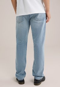 Lichtblauwe denim jeans met een recht gesneden pijp, voorzien van achterzakken en subtiele vervaging, gecombineerd met zwarte schoenen.