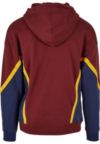 Sweat à capuche couleur marron foncé avec une texture douce, présentant un motif en biais bleu marine et jaune sur les côtés et une capuche à cordon de serrage.