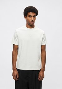 Biała t-shirt z okrągłym dekoltem wykonana z gładkiej bawełny. Krótkie rękawy, minimalne logo na piersi, luźny krój, w połączeniu z czarnymi spodniami.