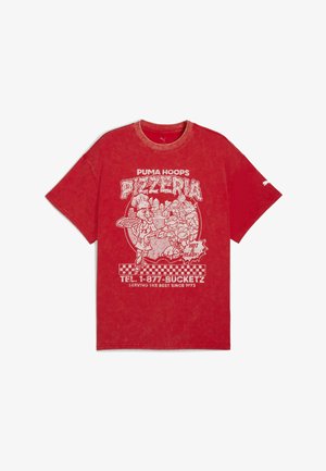 Vörös pamut póló nagy fehér grafikával, amely pizzát és kosárlabdát ábrázol, sakktáblaszerű kerettel és markáns felirattal.