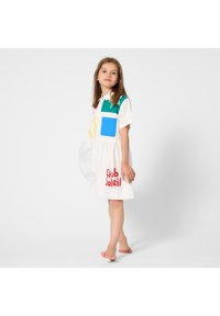 Άσπρο φόρεμα με κοντά μανίκια, διακοσμημένο με πολύχρωμες πατς σε μπλε, πράσινο και κίτρινο, με την ένδειξη «Club Soleil» τυπωμένη με κόκκινα γράμματα στη φούστα.