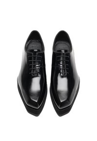 Zwarte leren schoenen met een glanzende afwerking, spitse neuzen en een vetersluiting met zes oogjes. De zool is dik en lichtjes gestructureerd.